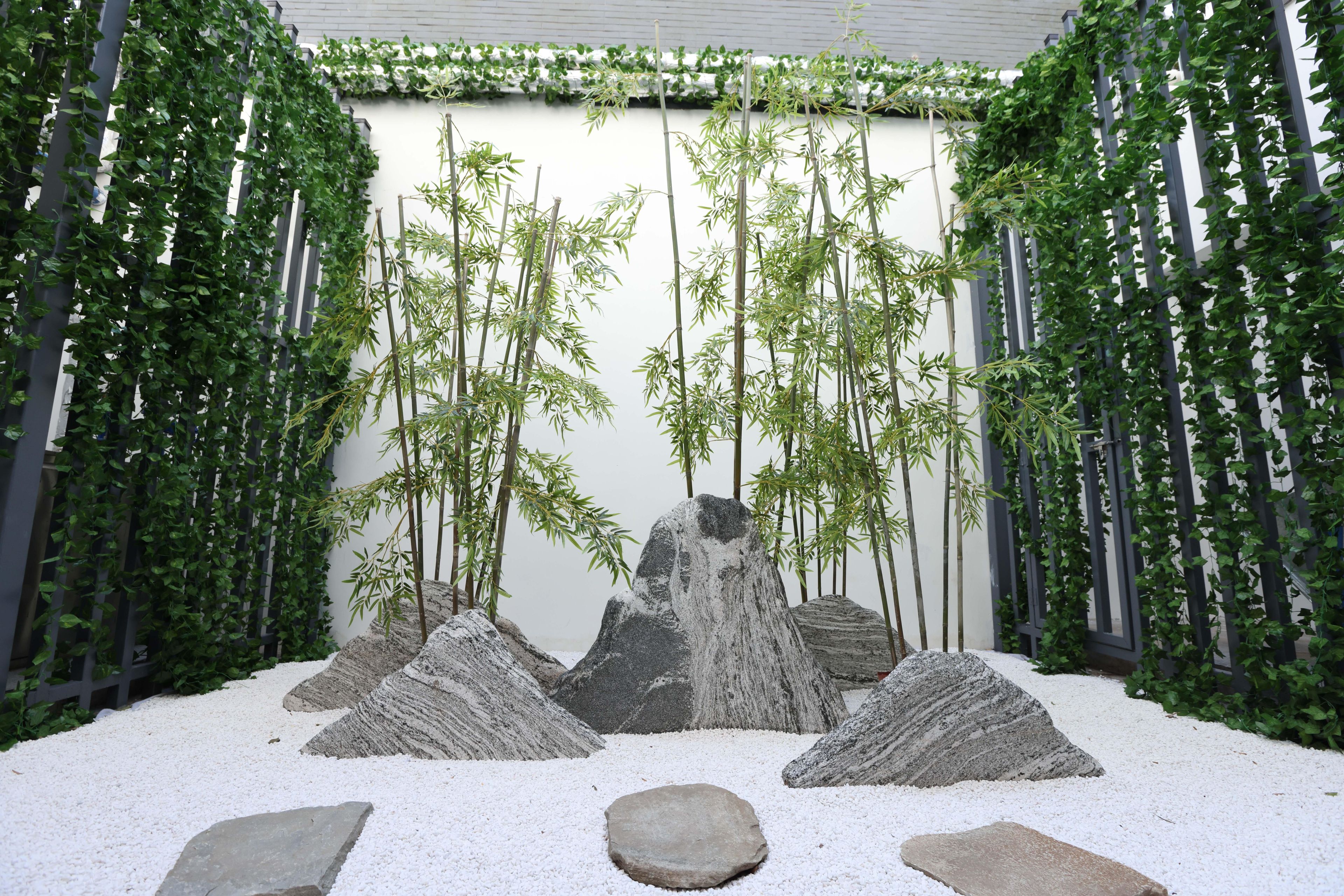 Een zen-tuin met rotsformaties, bamboe en een pad van wit grind.