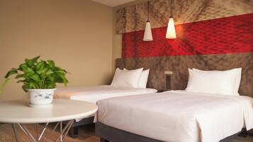 A hotel room with two beds, a small round table with a potted plant, and a red and beige textured wall.