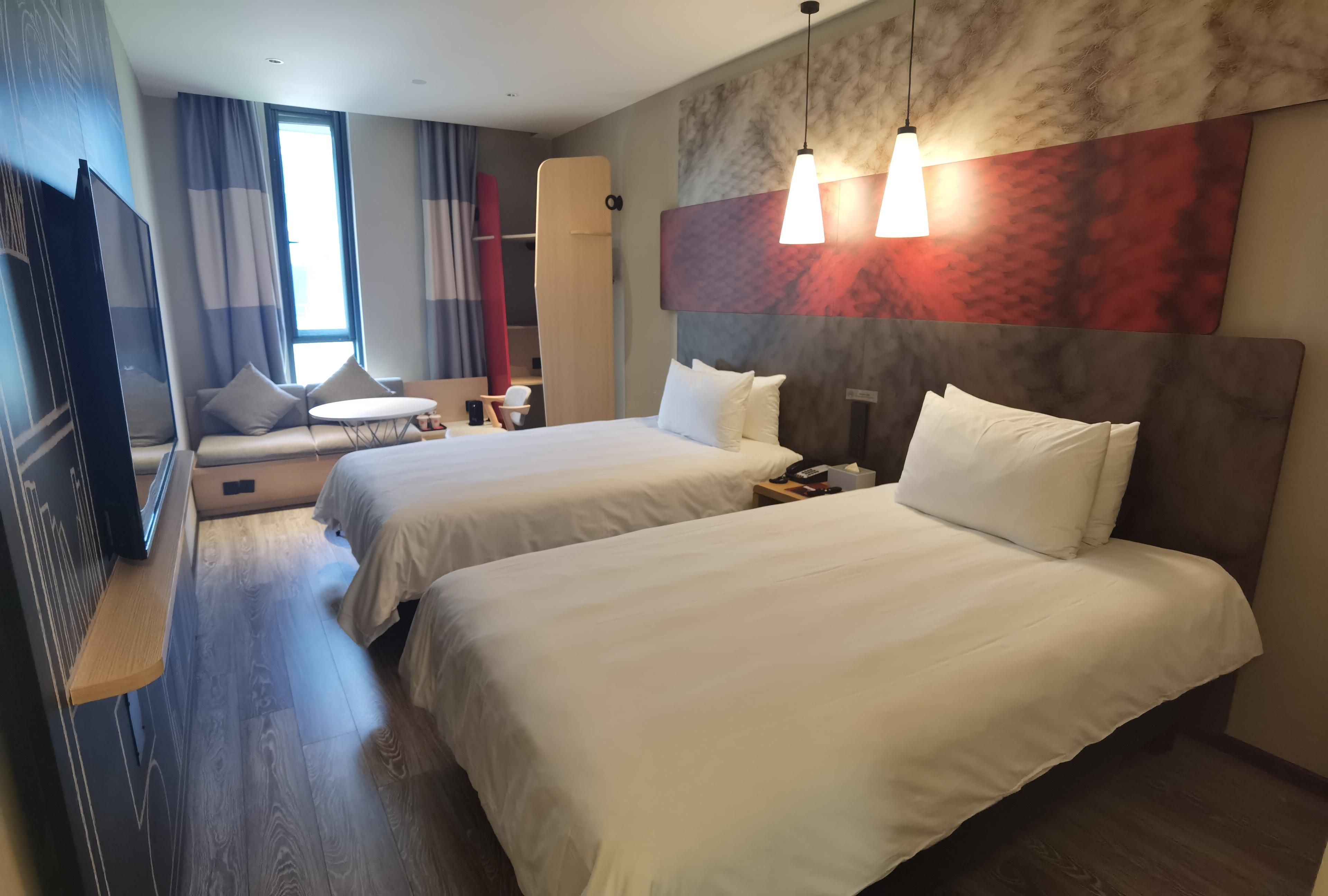 A hotel room with two beds, a TV, a desk, and a chair.