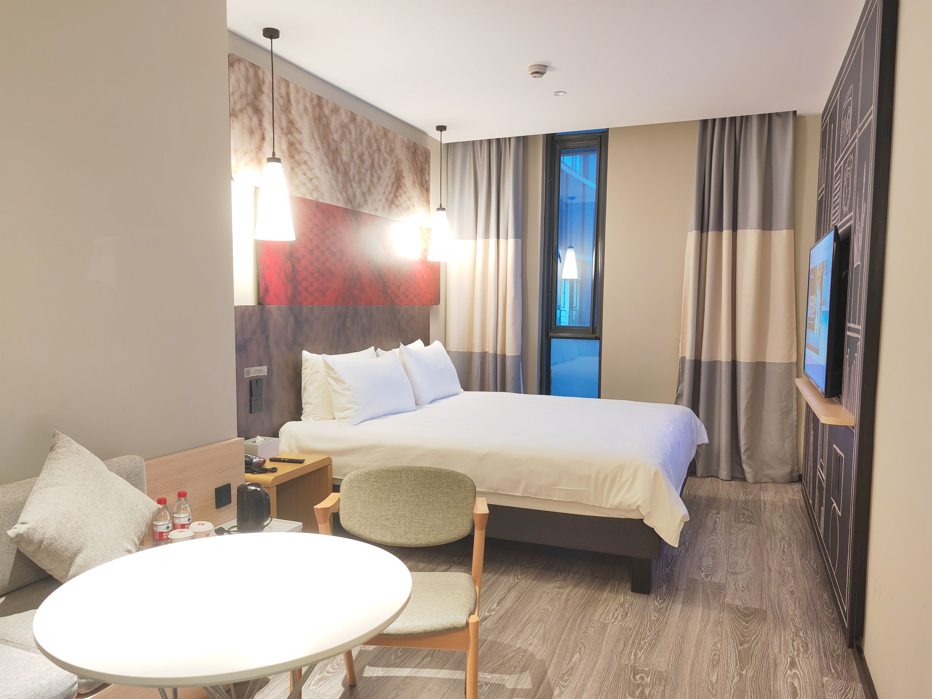 A hotel room with a bed, a table, a chair, a TV, and a window.