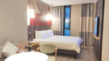 A hotel room with a bed, a table, a chair, a TV, and a window.