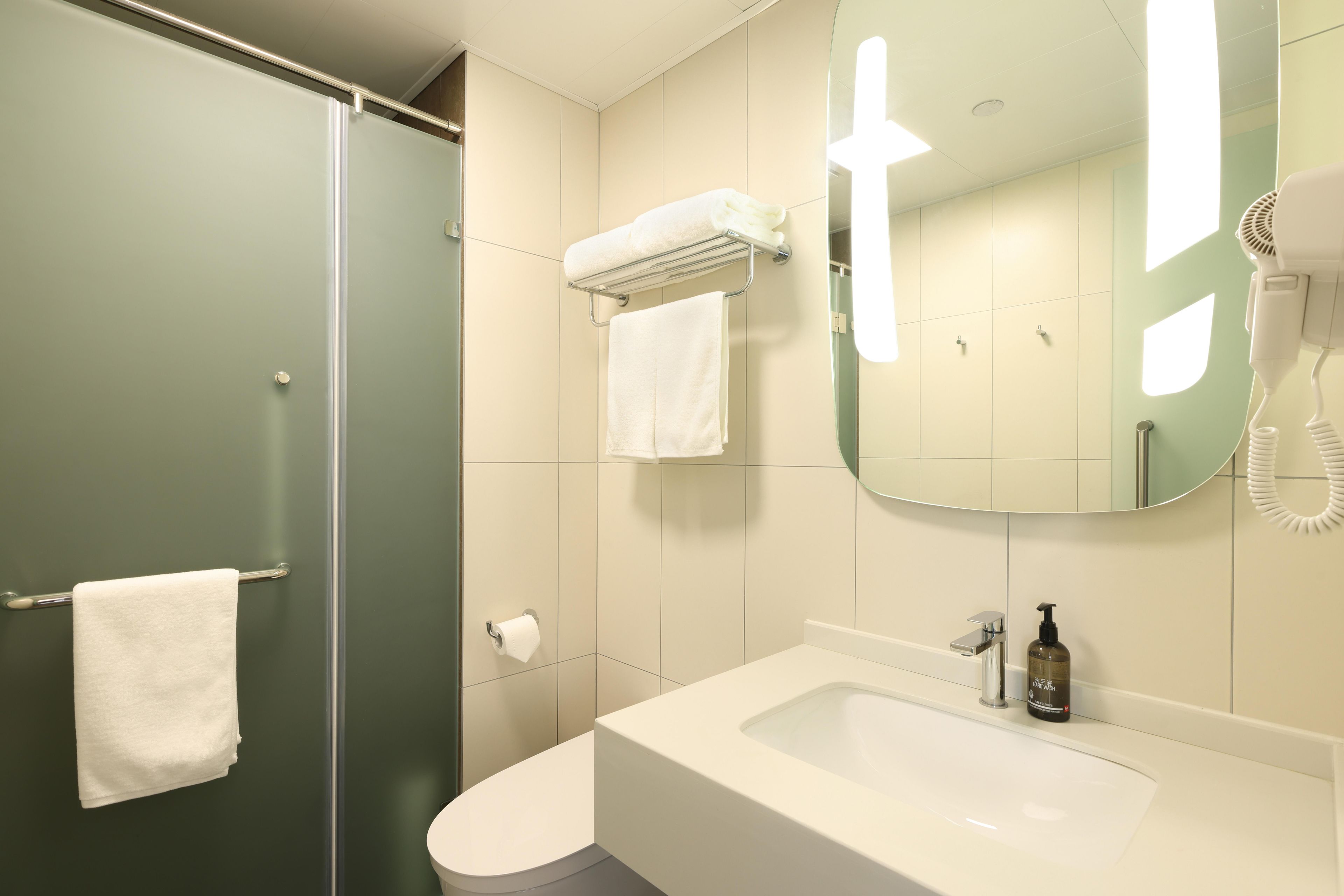 A bathroom with a glass shower door, a white sink, a mirror, and a towel rack.
