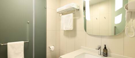 Bany amb porta de dutxa de vidre, un lavabo blanc, un mirall i una barra de tovalloles.