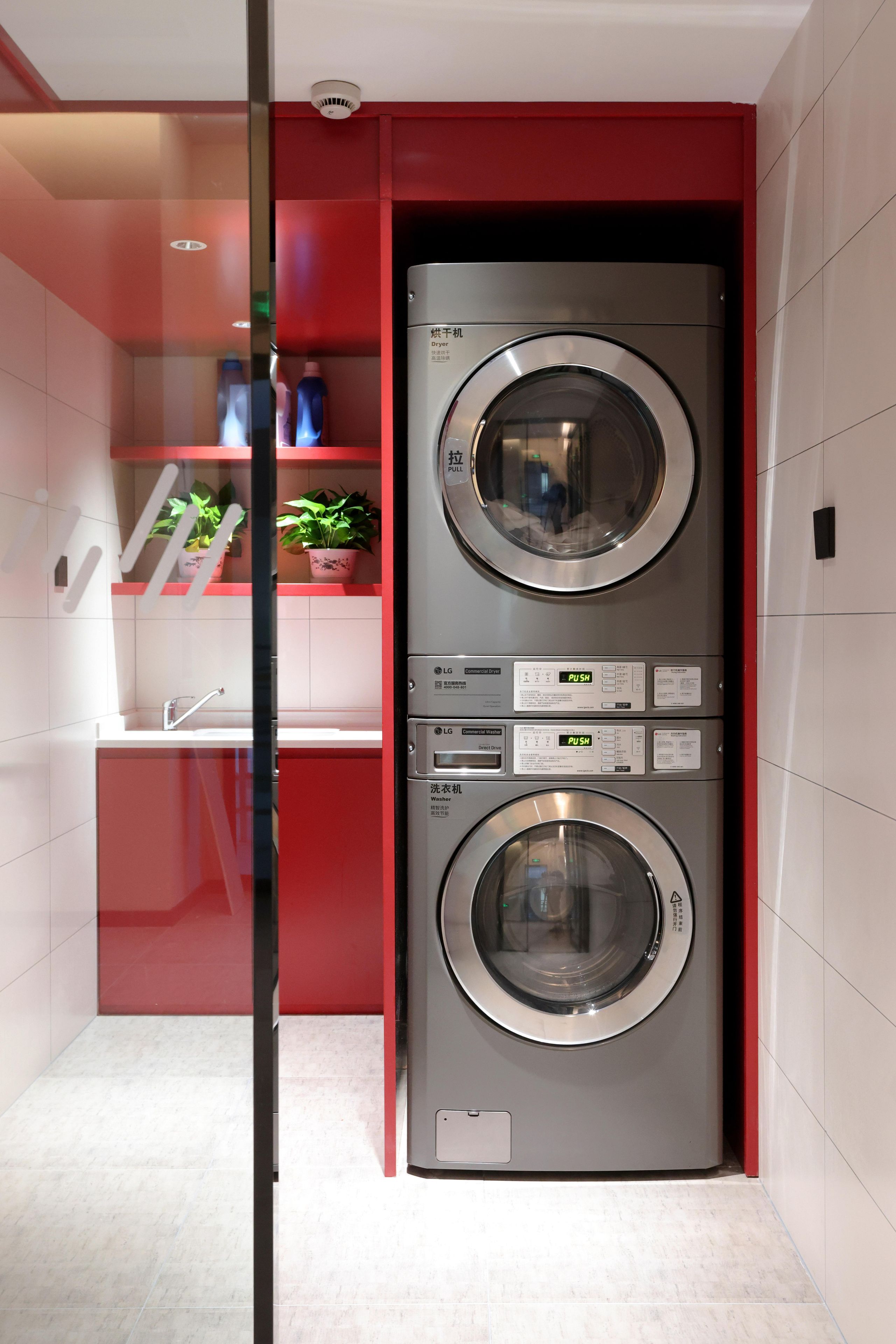 A compact laundry room with two stacked washing machines, a sink, and a potted plant.