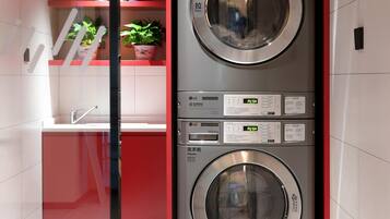 A compact laundry room with two stacked washing machines, a sink, and a potted plant.
