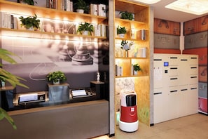 Un área de recepción con un quiosco digital, estanterías con plantas y una máquina de café.
