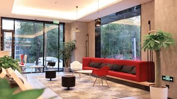 A modern lobby with a red sofa, white chairs, a coffee table, and potted plants.