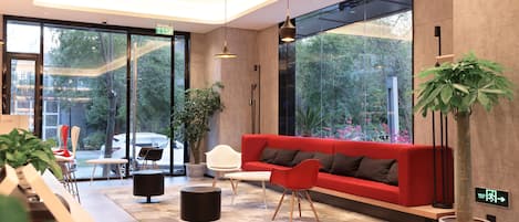 Een moderne lobby met een rode bank, witte stoelen, een bijzettafeltje en potplanten.