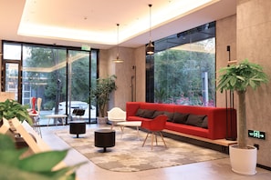 Un vestíbulo moderno con un sofá rojo, sillas blancas, una mesa de centro y plantas en macetas.