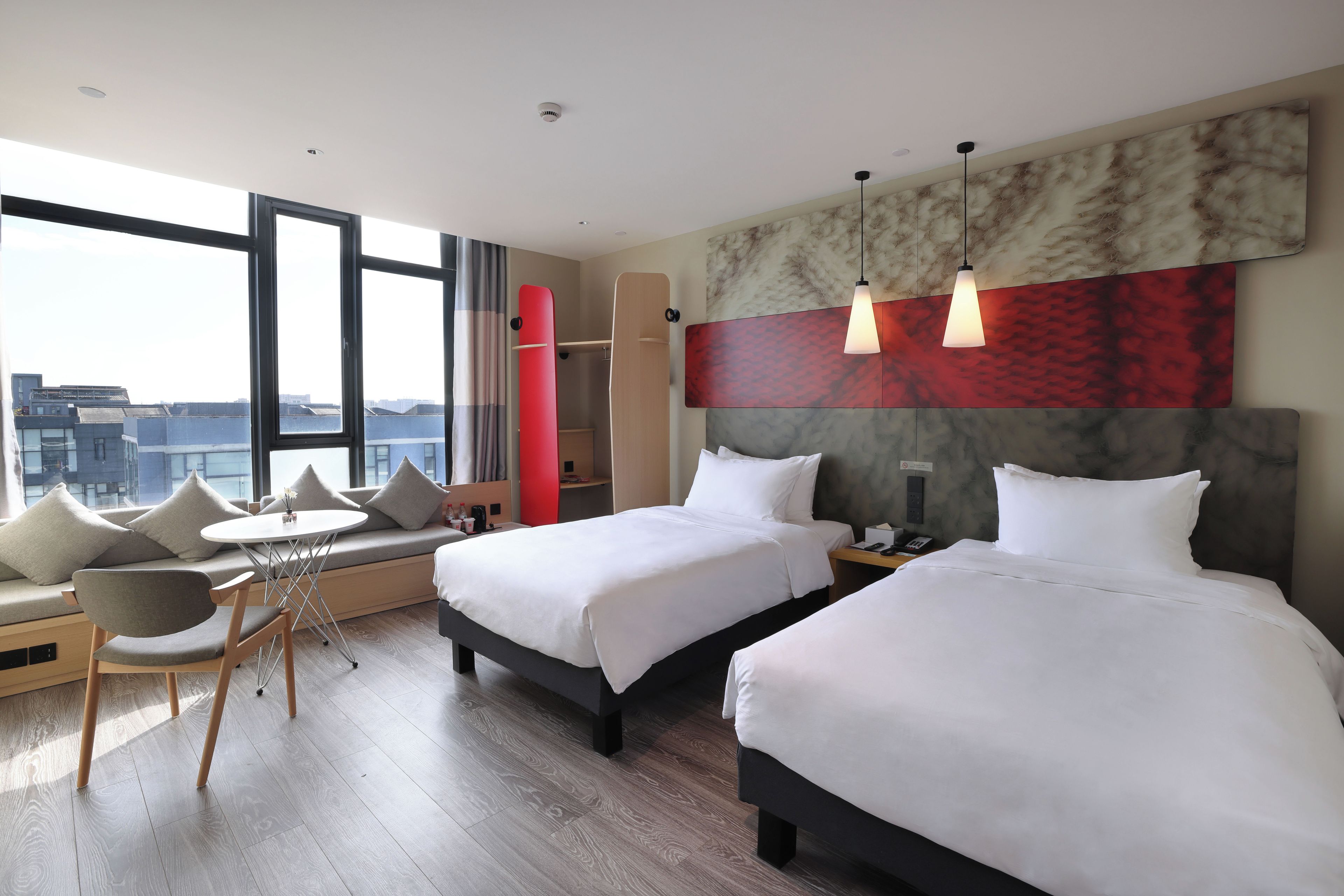 A hotel room with two beds, a sofa, a dining table, and a city view.