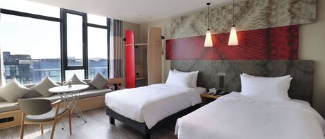 A hotel room with two beds, a sofa, a dining table, and a city view.