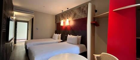 A hotel room with two beds, a round table, a chair, and a red accent wall.