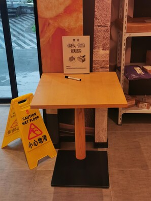 Una pequeña mesa de madera con base negra, un letrero de precaución indicando suelo mojado y un marcador sobre la mesa.