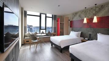 A hotel room with two beds, a seating area with a table, a large window, and a city view.
