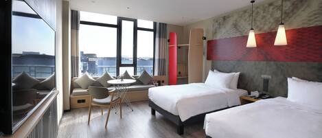 A hotel room with two beds, a seating area with a table, a large window, and a city view.