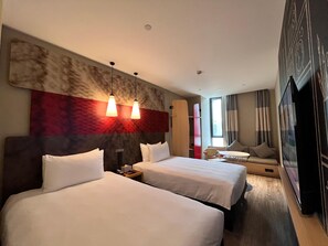 Habitación de hotel con dos camas, un sofá, un televisor y un ventanal grande.