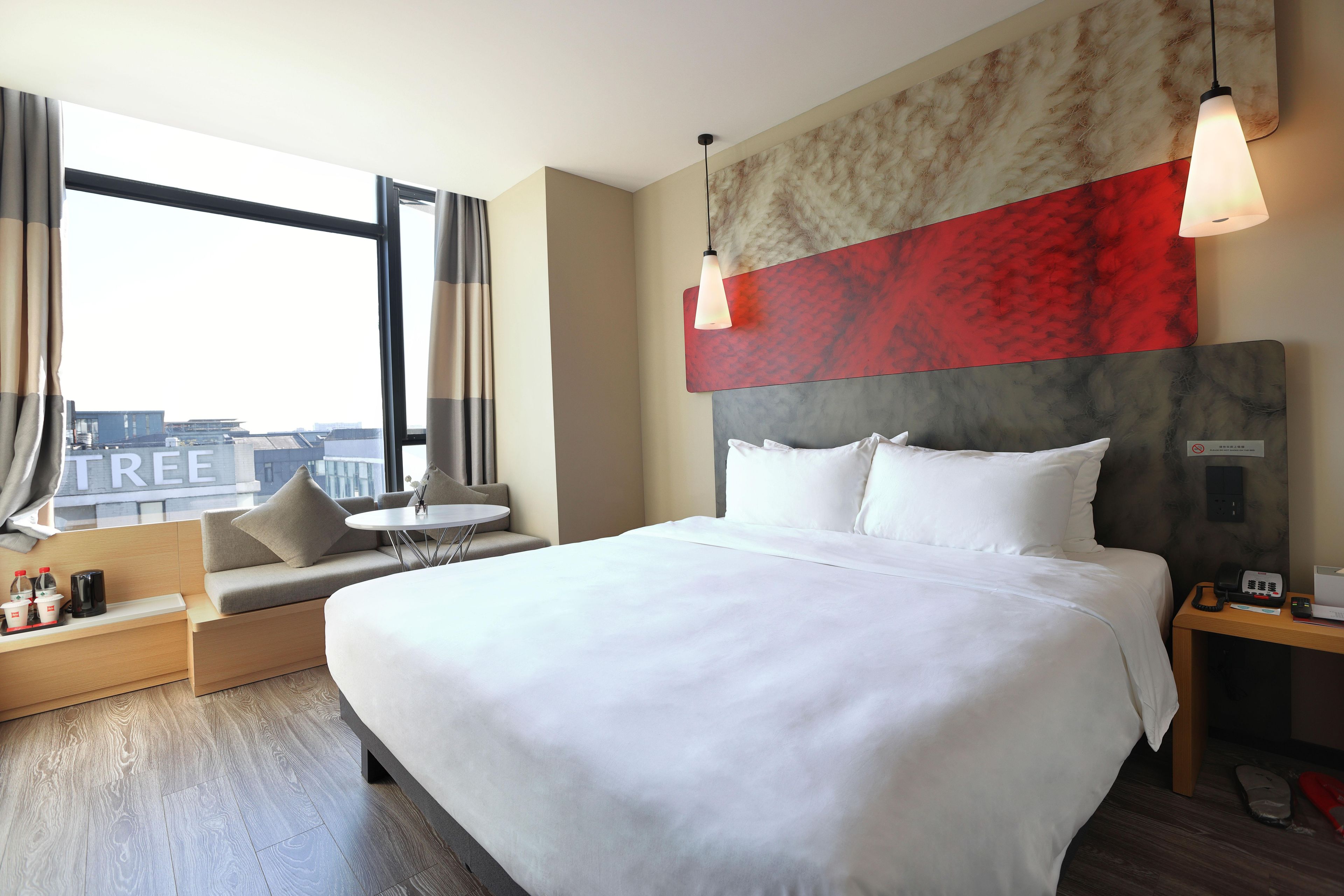 A hotel room with a large bed, a sofa, a small table, and a view of the city.