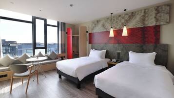 A hotel room with two beds, a sofa, a dining table, and a city view.