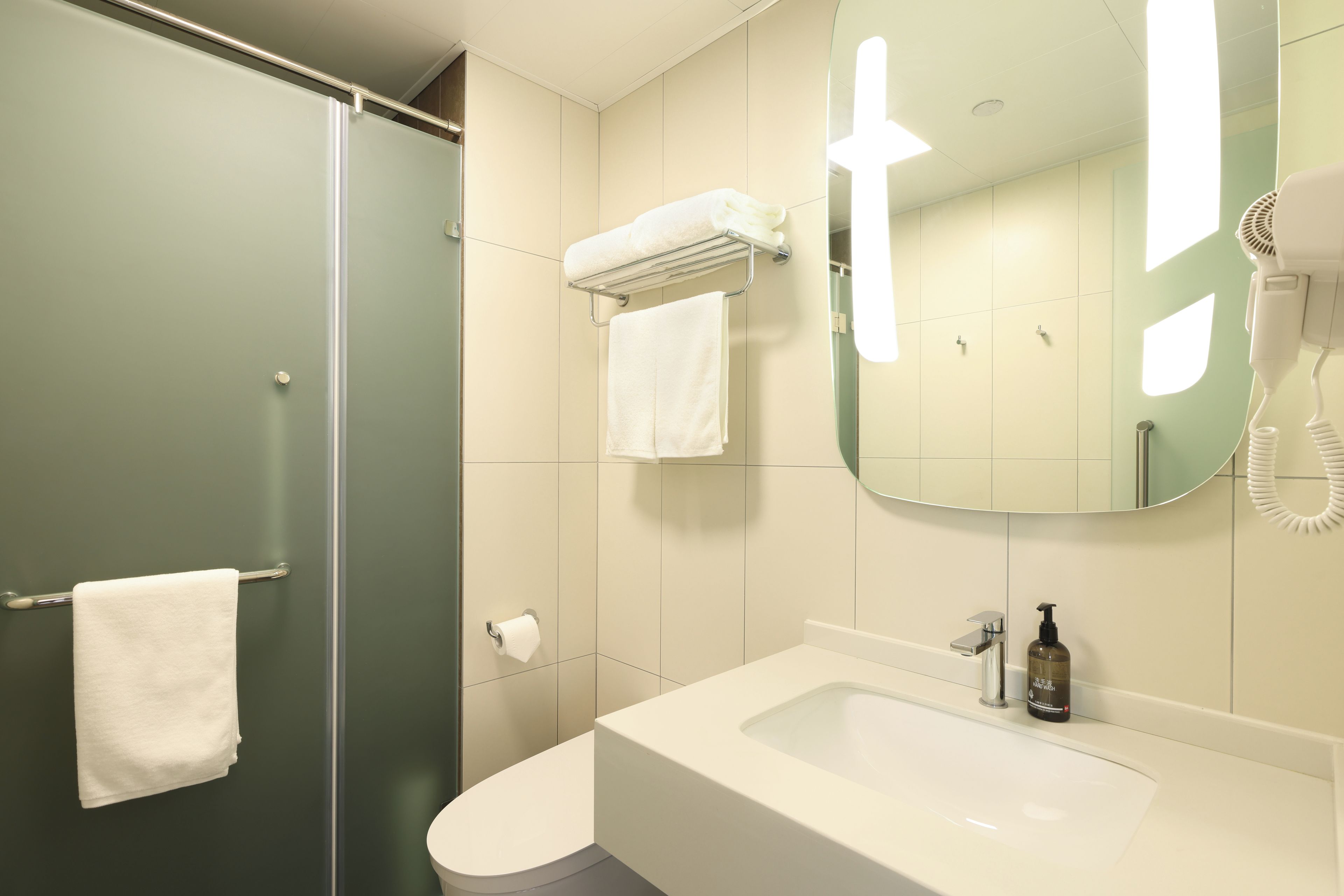 A bathroom with a shower, toilet, sink, and a mirror.