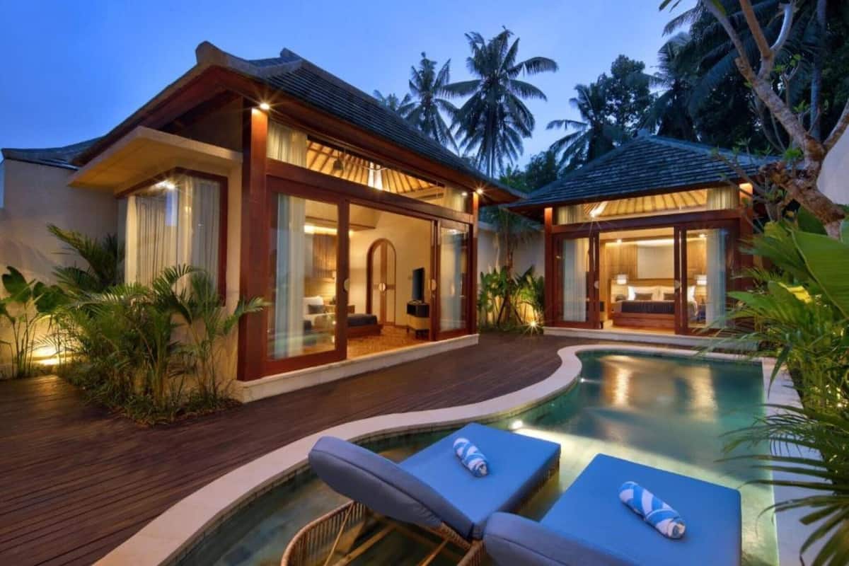 A resort with a swimming pool, wooden deck, and glass-enclosed rooms.
