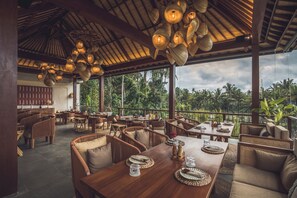 An outdoor restaurant with wooden furniture, hanging light fixtures, and a view of lush greenery. - Asvara Luxury Resort Ubud By Ini Vie hospitality (Payangan)
