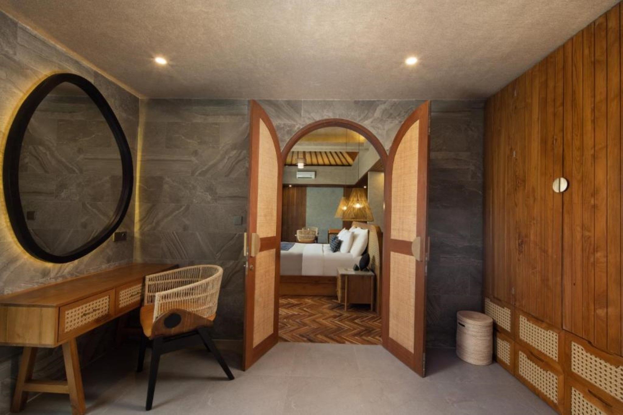 Ein Zimmer mit Bett, Schreibtisch und Stuhl, mit Blick in ein weiteres Zimmer durch eine geöffnete Tür.