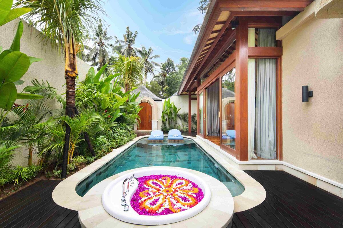 A swimming pool with a flower arrangement, surrounded by lush greenery and a wooden deck.