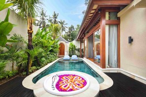 A swimming pool with a flower arrangement, surrounded by lush greenery and a wooden deck. - Asvara Luxury Resort Ubud By Ini Vie hospitality (Payangan)