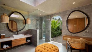 A modern bathroom with a glass shower, a round mirror, and a wooden vanity. - Asvara Luxury Resort Ubud By Ini Vie hospitality (Payangan)