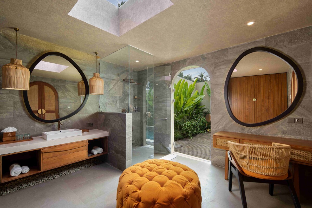 A modern bathroom with a glass shower, a round mirror, and a wooden vanity.