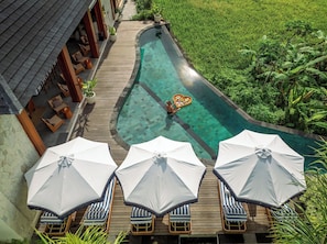 A pool with a wooden deck, lounge chairs, and umbrellas.