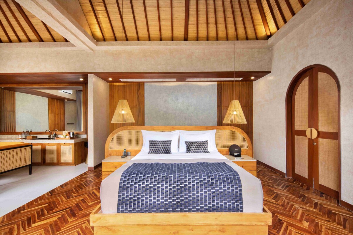 A hotel room with a wooden bed, a wooden floor, a large mirror, a wooden door, and a wooden ceiling.