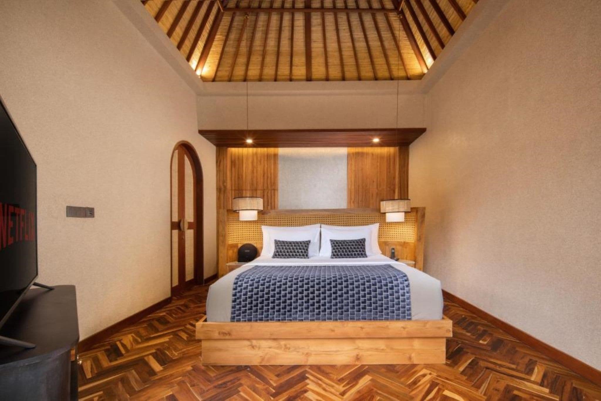 A bedroom with a wooden headboard, a bed with a patterned bedspread, and a herringbone-patterned floor.