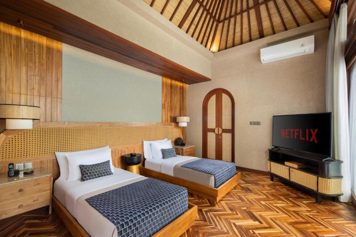 A hotel room with two beds, a television, and a wooden ceiling.