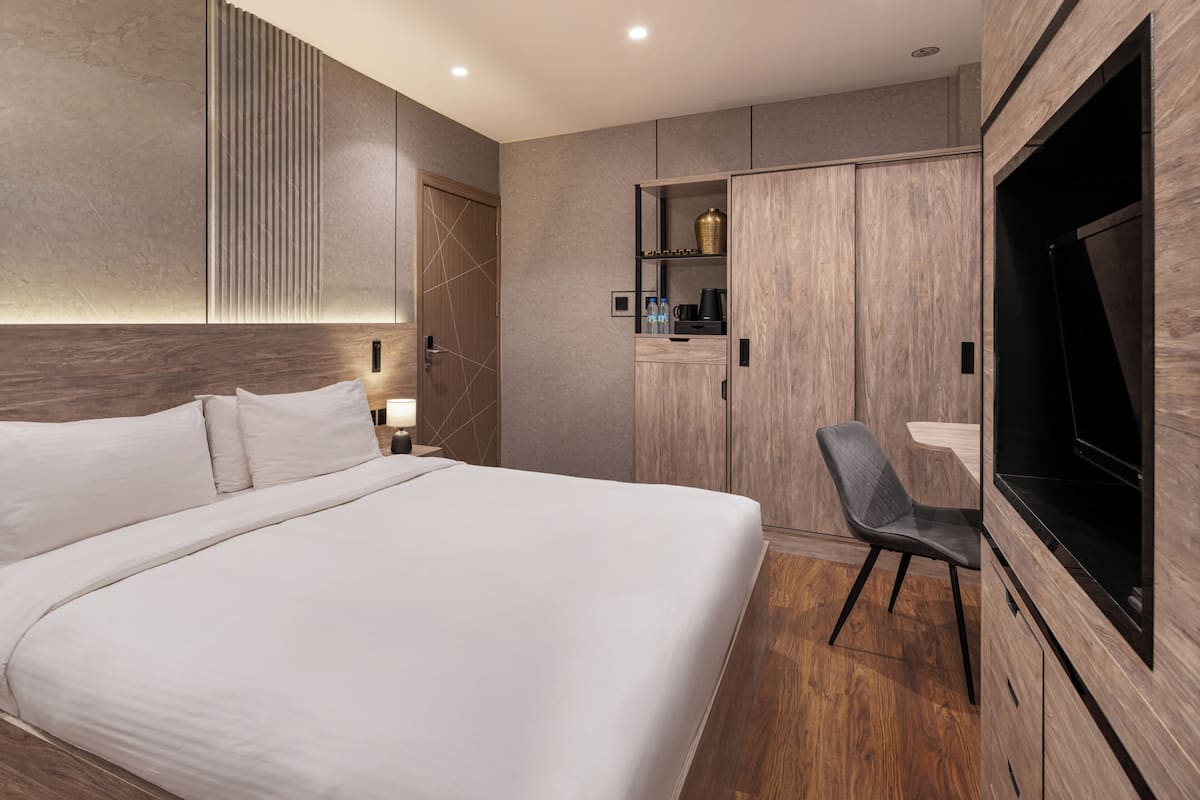 A modern hotel room with a large bed, a TV, a wardrobe, and a desk area.