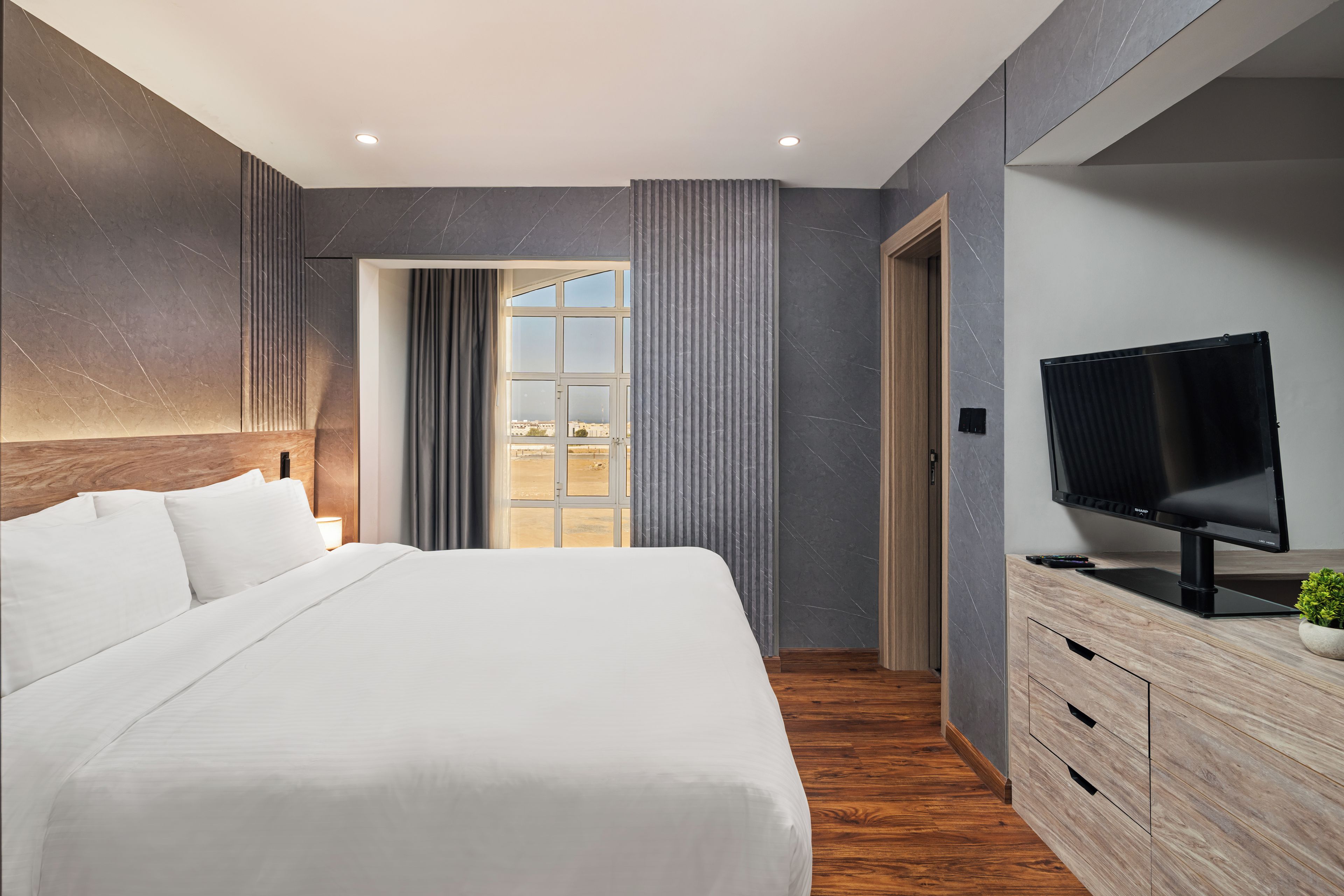 Una habitación de hotel moderna con una cama grande, televisión, cómoda de madera y vistas a la ciudad.