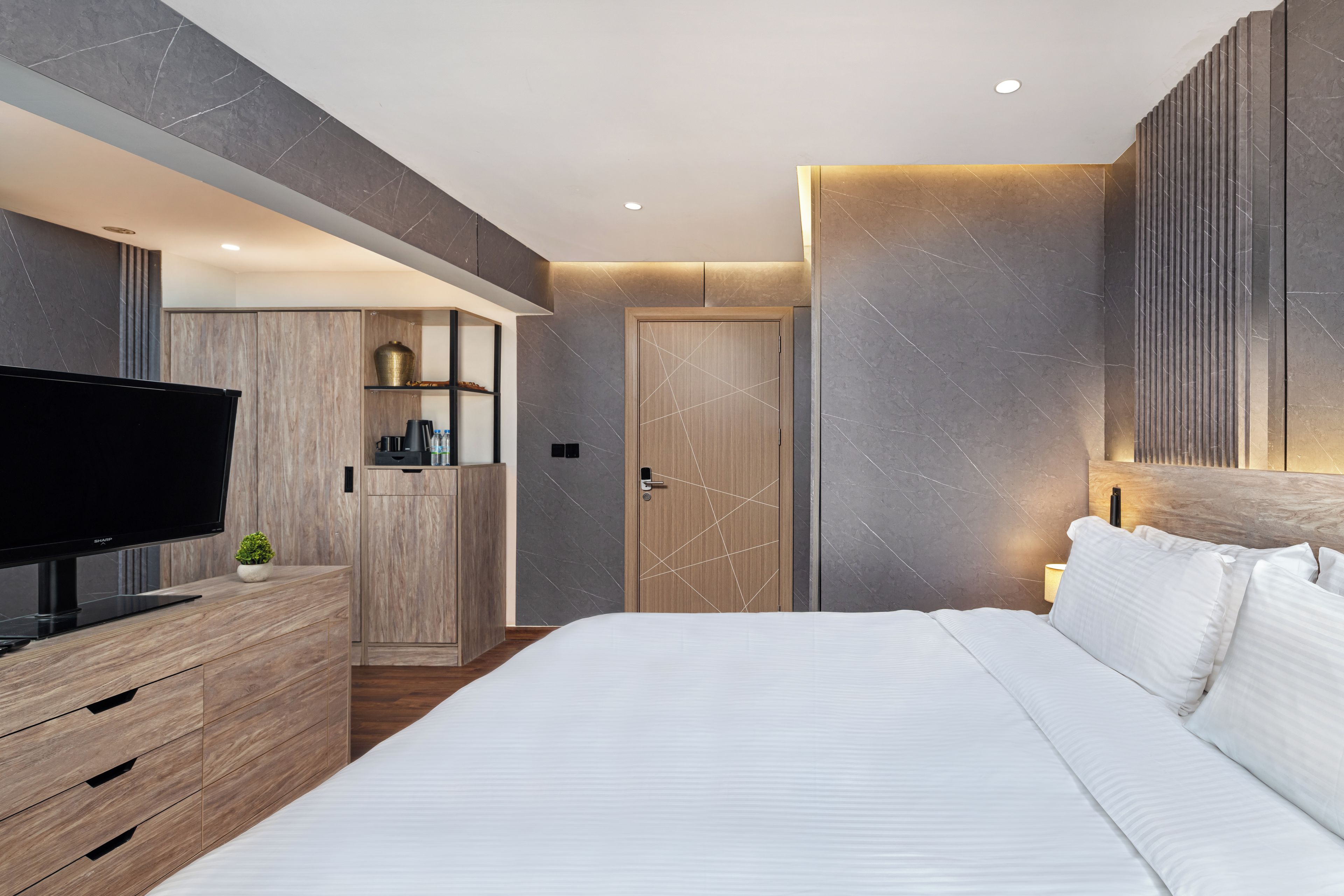 A modern bedroom with a large bed, a TV on a wooden dresser, a wardrobe, and a door with a geometric design.