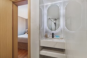 A modern bathroom with a marble vanity, a large mirror, and a shower area. - Regency Inn Hotel Oman (Muscat)