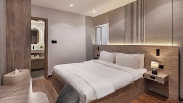 Una habitación de hotel moderna con una cama grande, mesita de noche con lámpara, un escritorio pequeño y una silla.