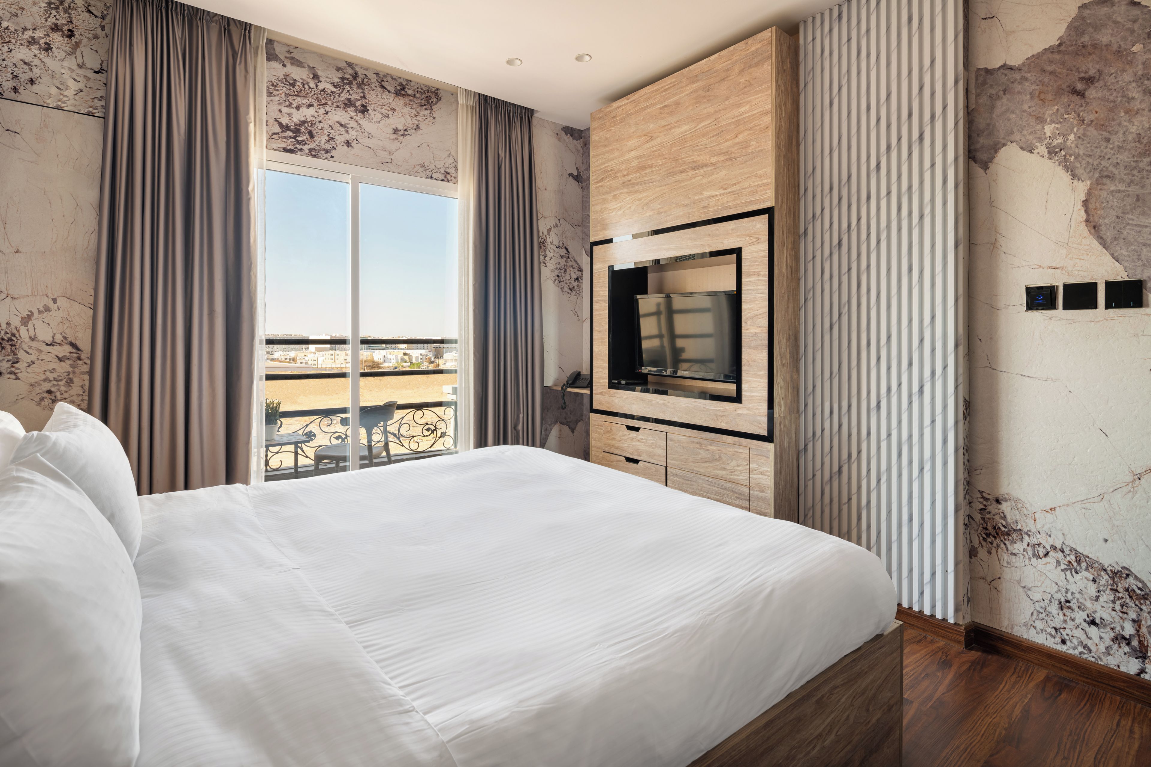 A modern hotel room with a large bed, a TV, and a balcony with a view.