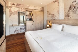 A modern hotel room with a large bed, a wooden wardrobe, a vanity with a mirror, and a marble wall. - Regency Inn Hotel Oman (Muscat)