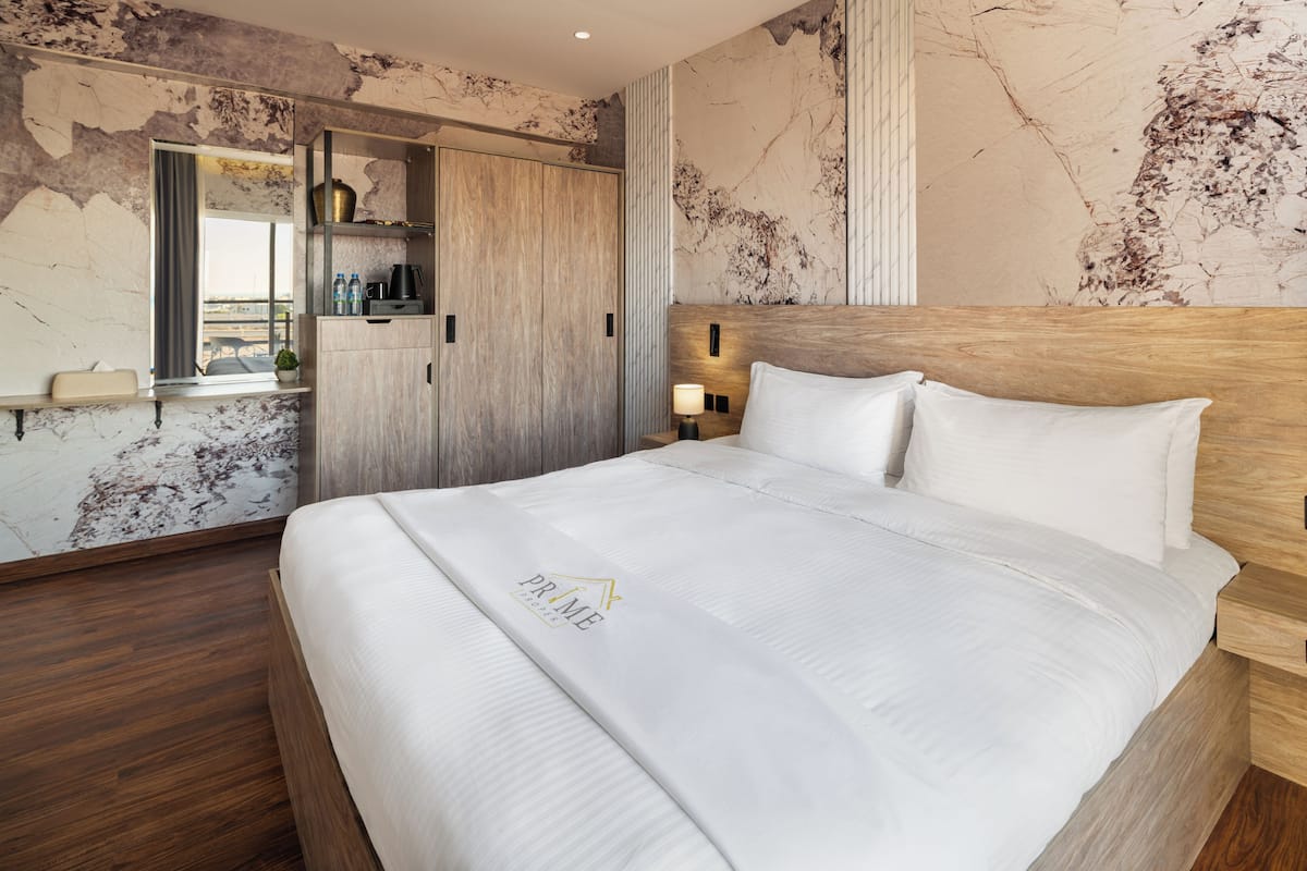 Habitación de hotel con una cama grande, cabecero de madera, armario empotrado, mesita de noche con lámpara y pared de mármol.