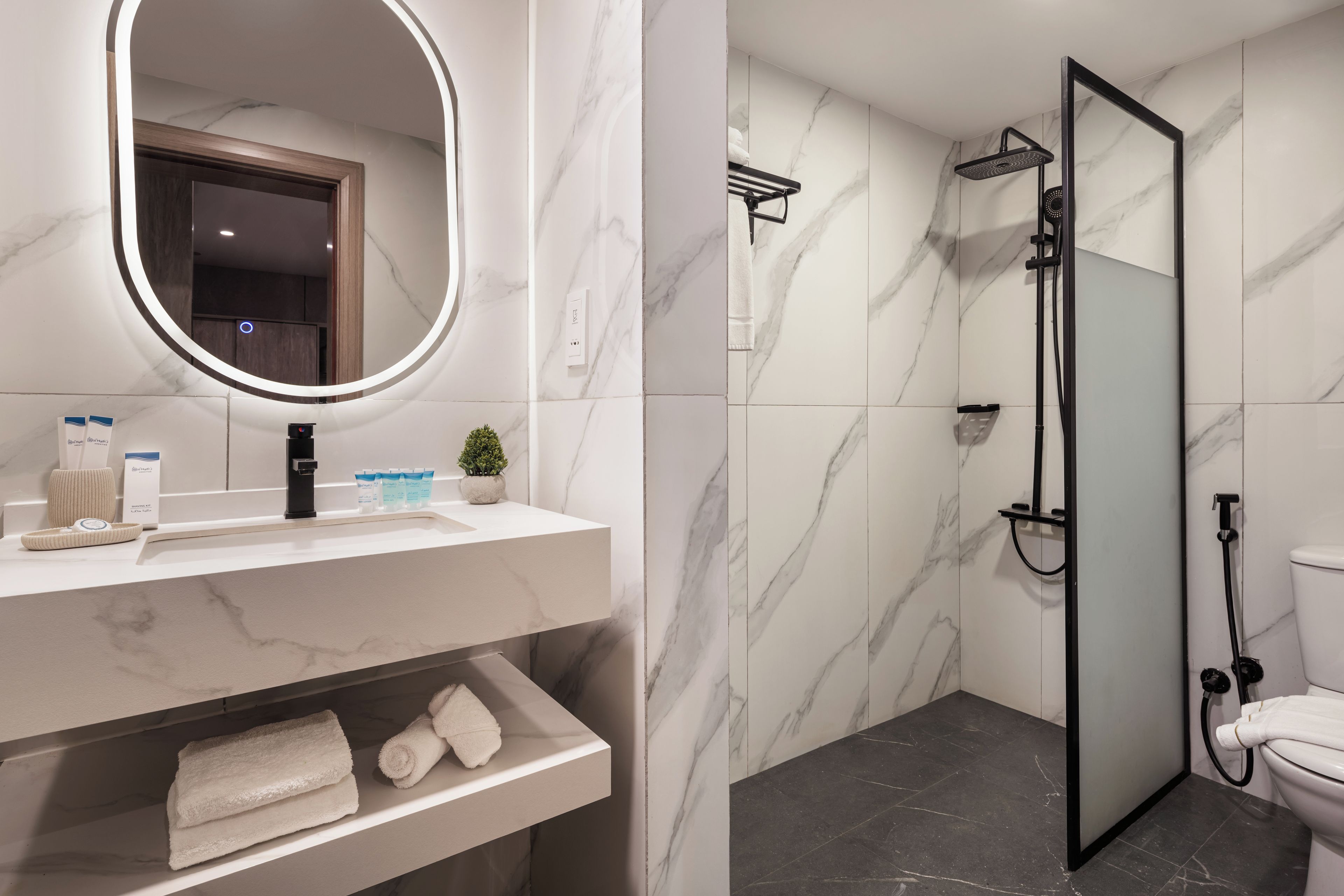A bathroom with a marble vanity, a round mirror, a shower enclosure, and a toilet.