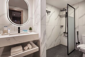 A bathroom with a marble vanity, a round mirror, a shower enclosure, and a toilet. - Regency Inn Hotel Oman (Muscat)