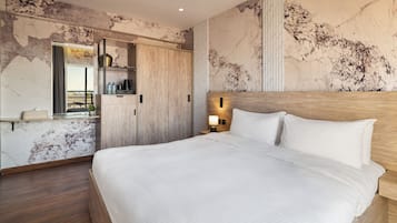A modern hotel room with a large bed, a wooden headboard, a nightstand with a lamp, a wardrobe, and a marble wall.