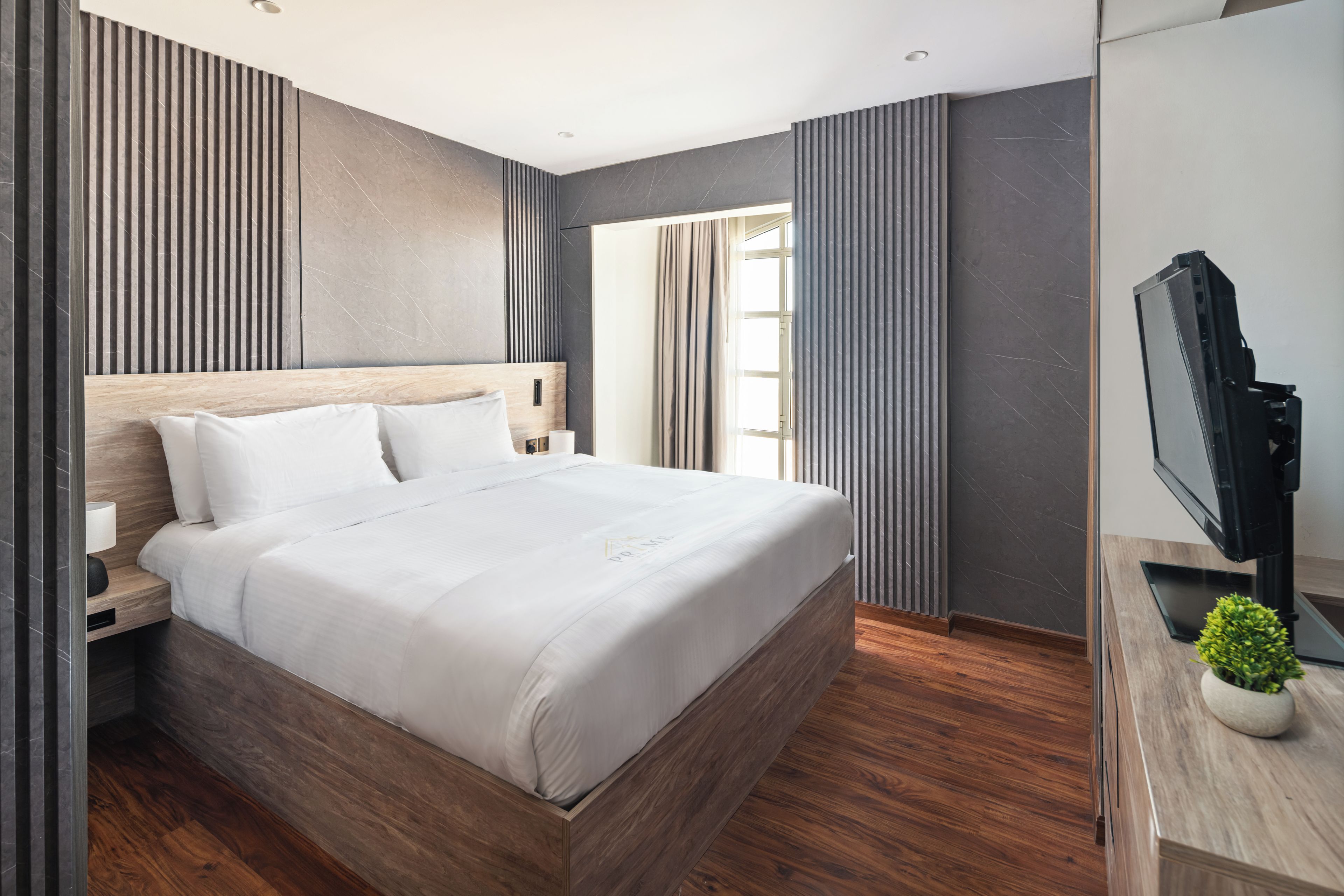 A modern hotel room with a large bed, wooden headboard, a flat-screen TV, and a small potted plant.