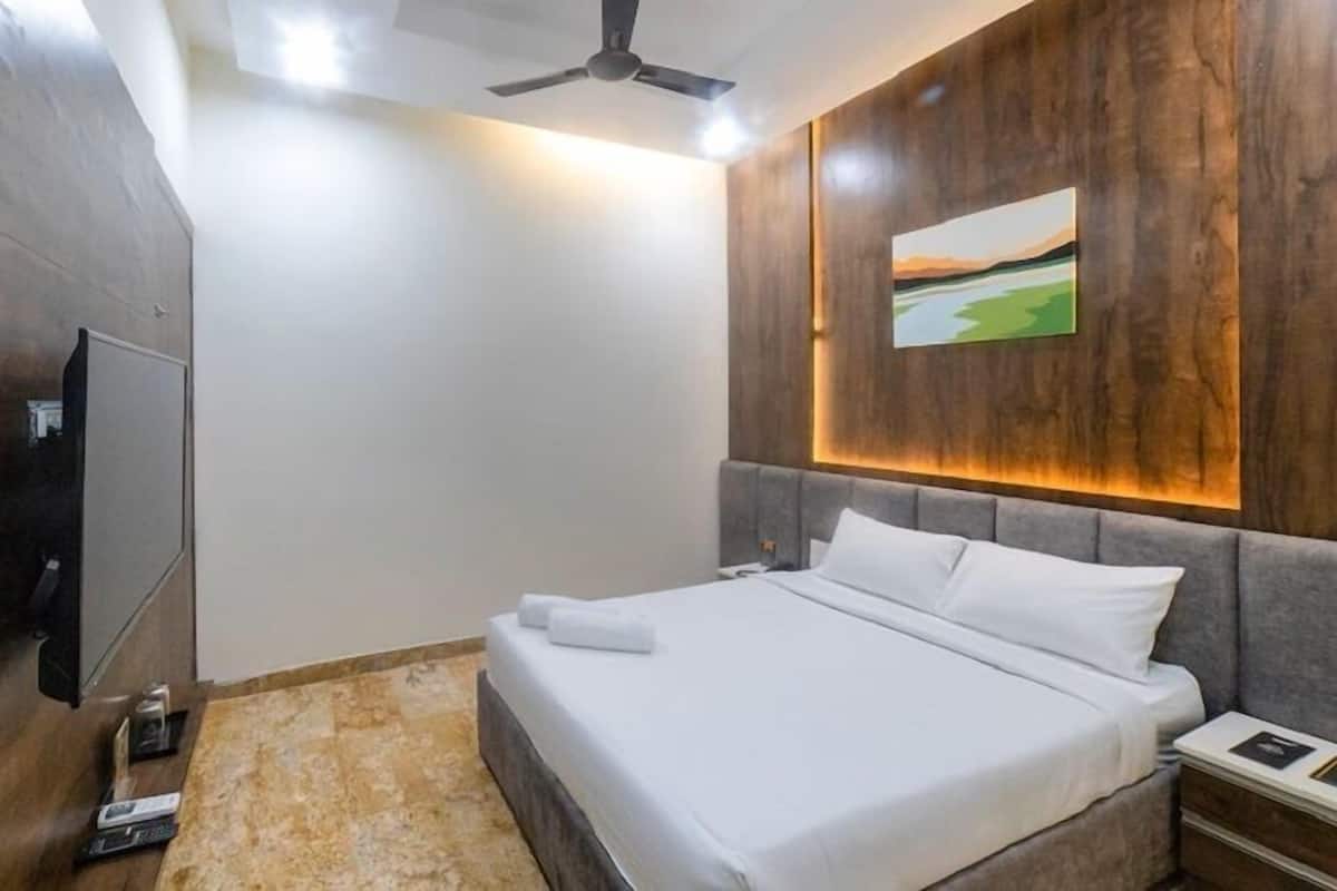 Una habitación de hotel con cama, televisión, ventilador de techo y un cuadro en la pared.