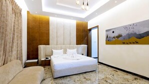 A bedroom with a bed, a nightstand, a chair, a painting, and a door. - Aara Jungle Resort (Mettupalayam)