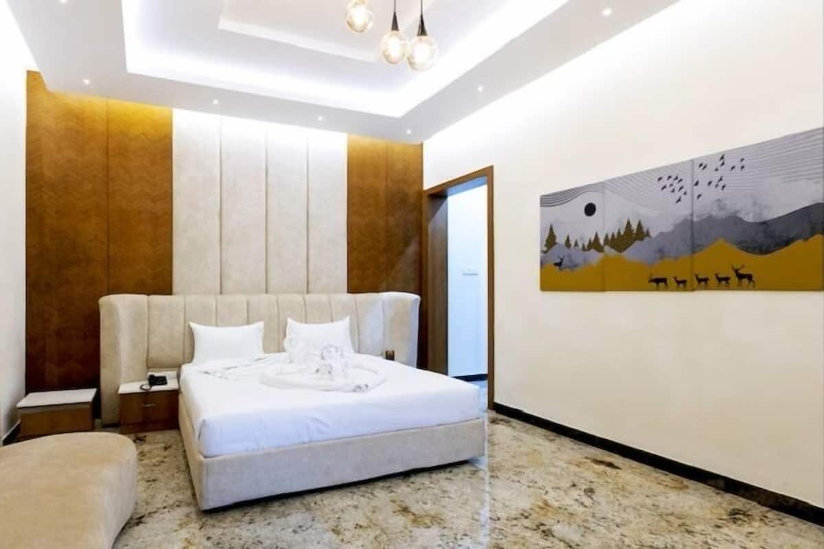 Un dormitorio con cama, mesita de noche, silla, un cuadro y una puerta.