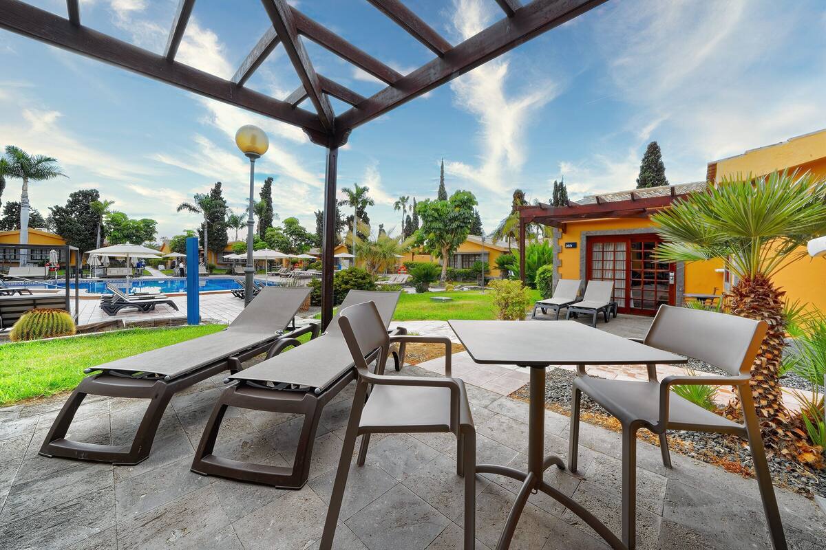 Eine Terrasse im Freien mit Liegestühlen und Tischen, im Hintergrund ein Pool und ein klarer Himmel.